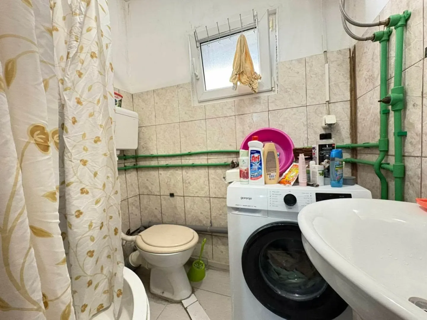 Manje kupatilo sa sanitarijama, veš mašinom i vidljivim instalacijama.
