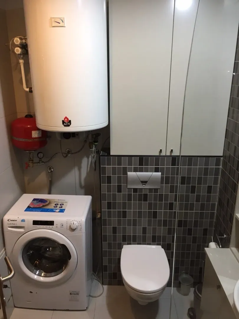 Manje kupatilo sa WC šoljom, veš mašinom i bojlerom.