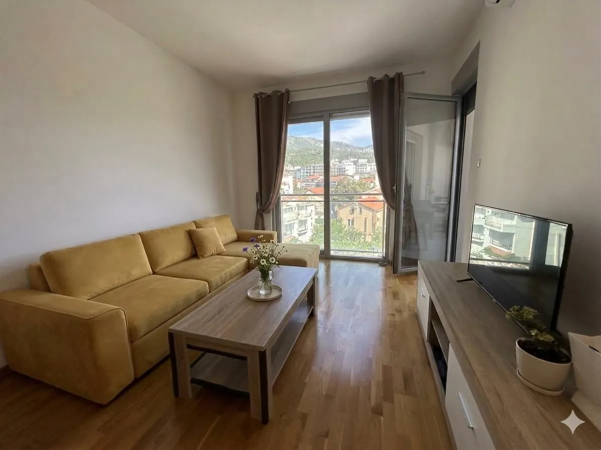 Dnevna soba sa garniturom, stočićem i televizorom, sa izlazom na terasu.