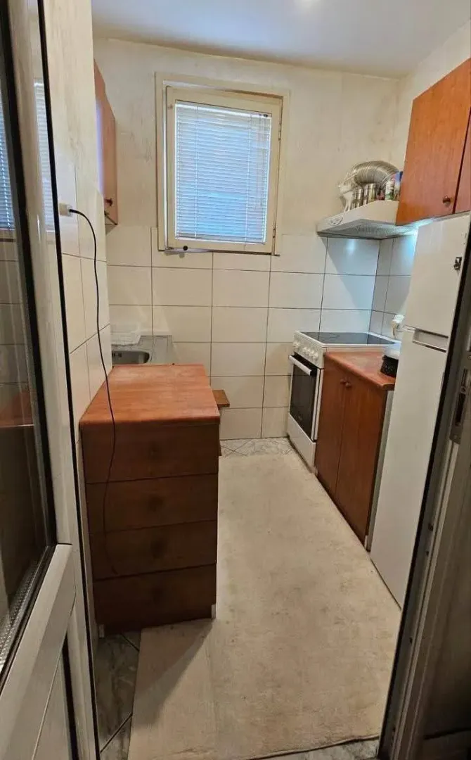 Manja kuhinja sa drvenim elementima, šporetom i frižiderom.