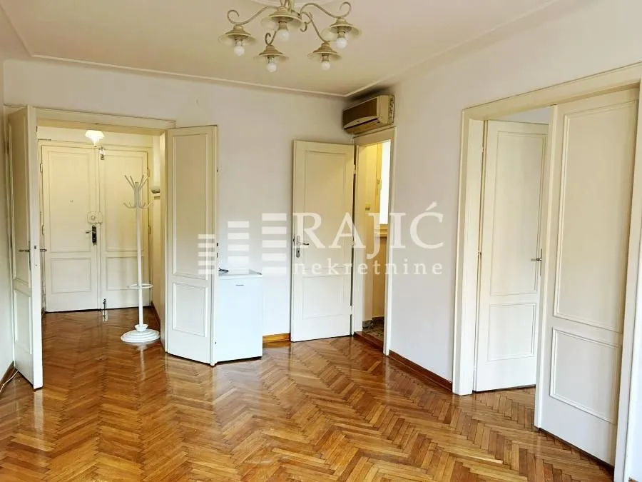 Spacious room with parquet flooring and multiple white doors.