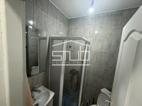 Small bathroom tiled in grey with a shower cabin and a washbasin. - image 7