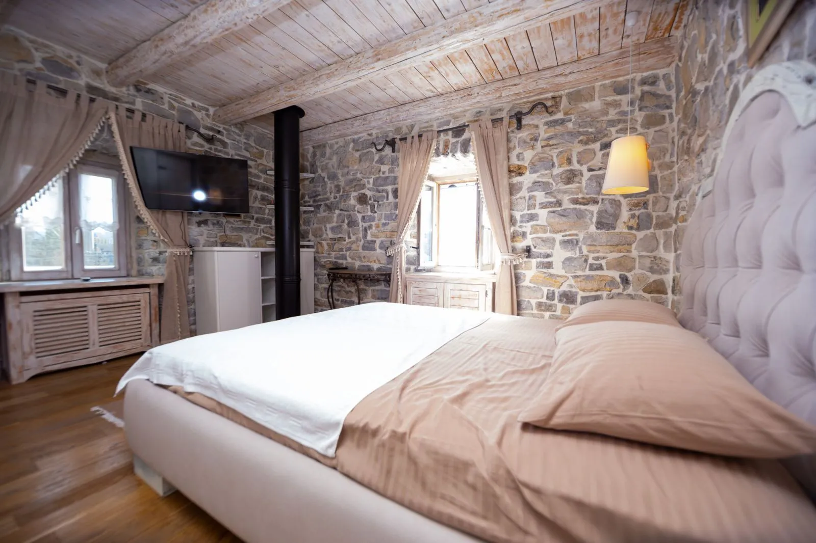 Rustic bedroom with stone walls and wooden ceiling.