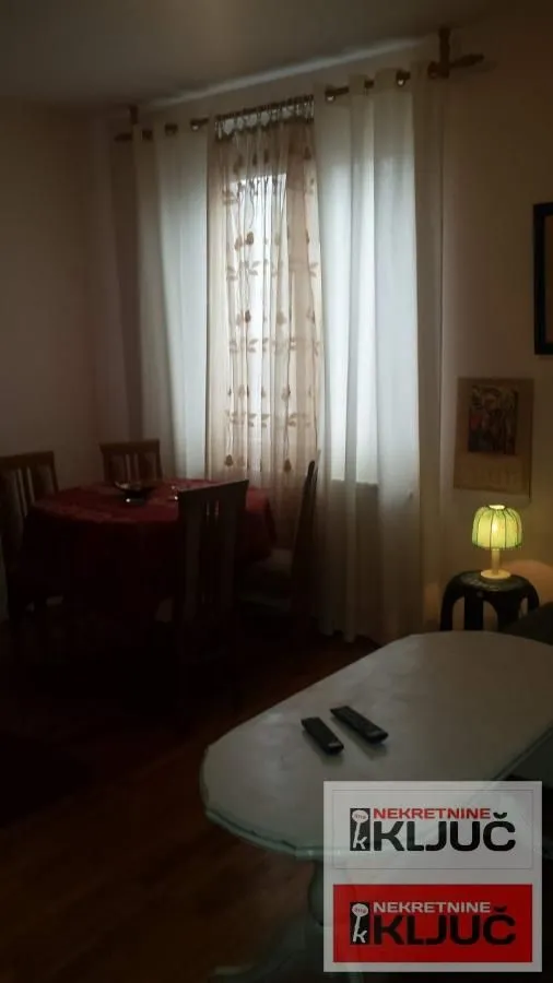 Dnevna soba sa trpezarijskim stolom i prozorom prekrivenim zavesama.