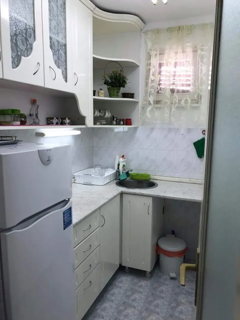 Manja bijela kuhinja sa sudoperom, frižiderom i visećim elementima.