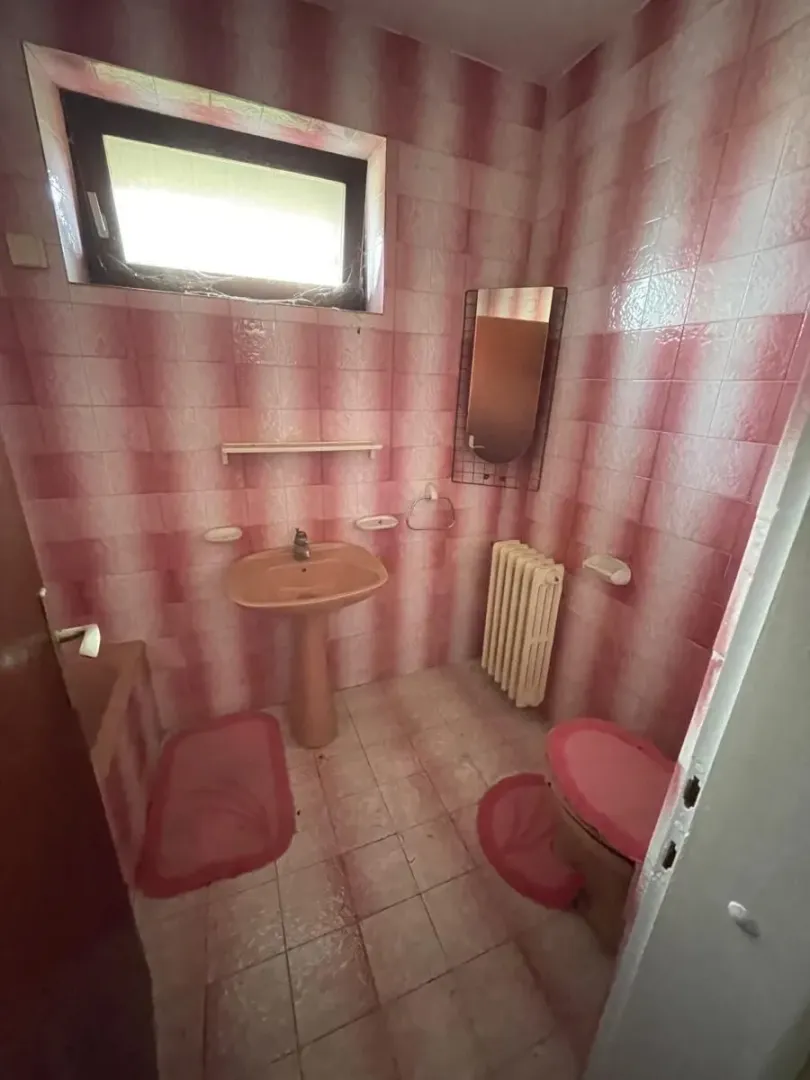 Starije kupatilo sa roze pločicama, umivaonikom i wc šoljom.