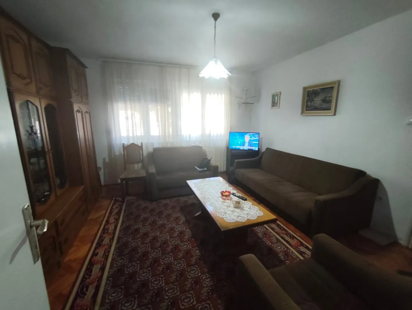 Nameštena dnevna soba sa garniturom i velikim drvenim ormanom.