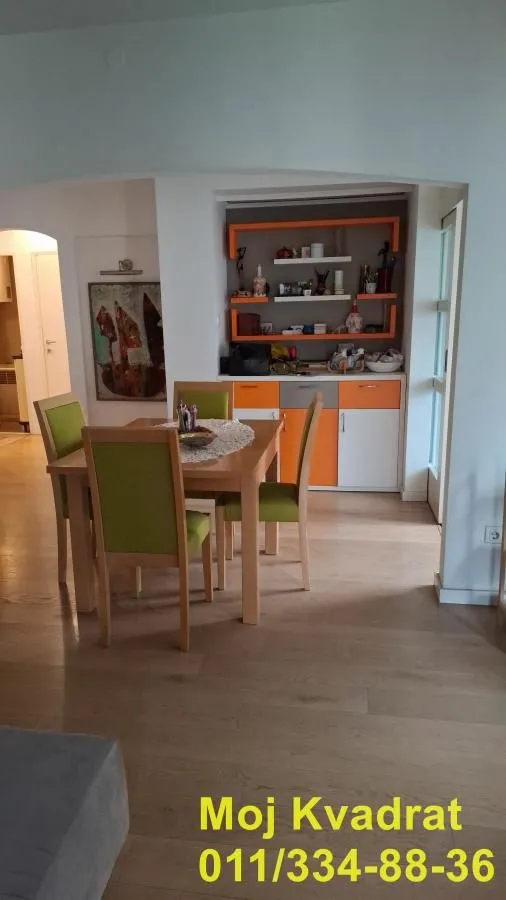 Trpezarija sa drvenim stolom i zelenim stolicama pored ugradne komode.