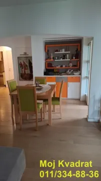 Trpezarija sa drvenim stolom i zelenim stolicama pored ugradne komode. - image 5