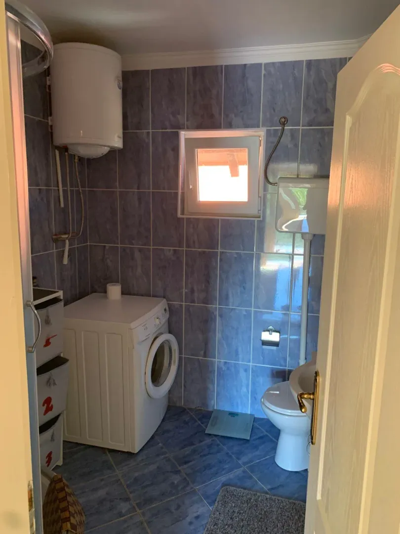 Small bathroom with blue tiles, shower, toilet, and washing machine.