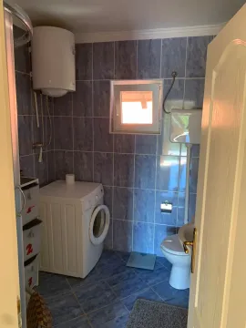 Small bathroom with blue tiles, shower, toilet, and washing machine. - image 8