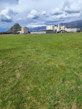 Prostrana zelena livada sa industrijskim objektima i planinama u pozadini. - image 9