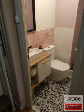 Manje kupatilo sa umivaonikom, toaletnom šoljom i dezeniranim pločicama na podu. - image 9