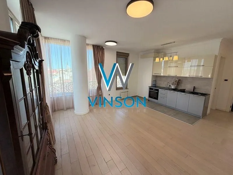 Living room with an open-plan kitchen and large windows.
