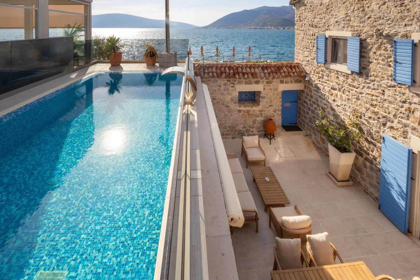 Terrace with a swimming pool and sea view in front of a stone house.