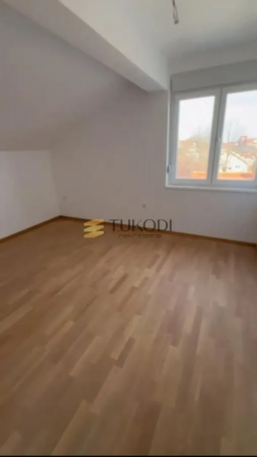 Prazna soba sa laminatnim podom i kosim plafonom.