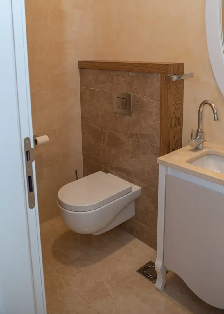 Smaller bathroom with a wall-hung toilet, vanity sink, and beige tiles.