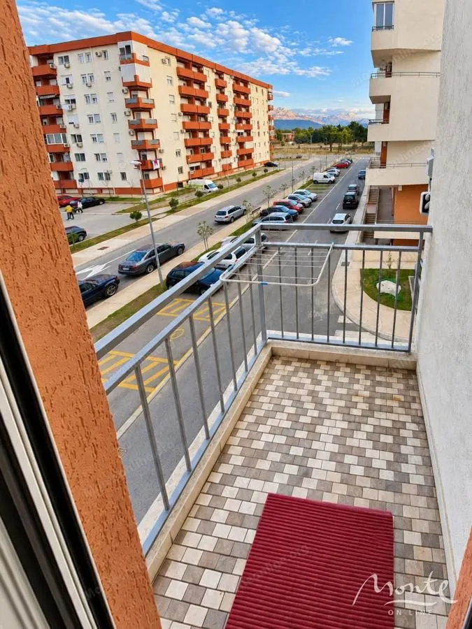 Pogled sa balkona na okolne zgrade i ulicu sa parkingom.