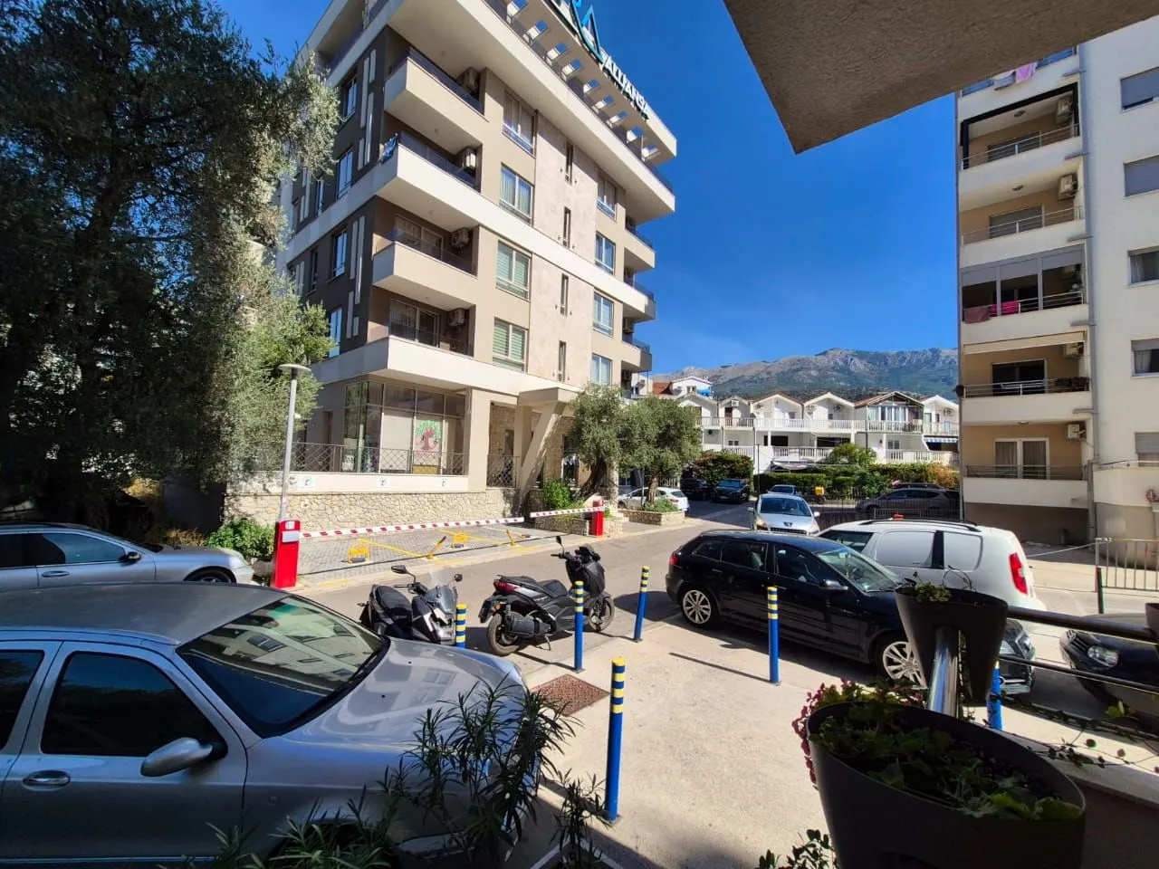 Pogled sa terase na zgradu, dvorište i parking ispred objekta.