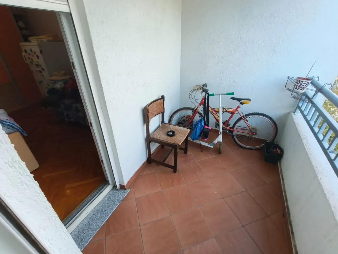 Natkriveni balkon sa stolicom, biciklom i trociklerom.