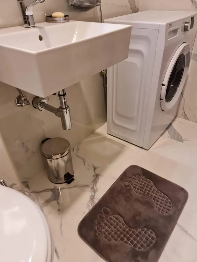 Kupatilo sa umivaonikom, veš mašinom i mermernim pločicama.