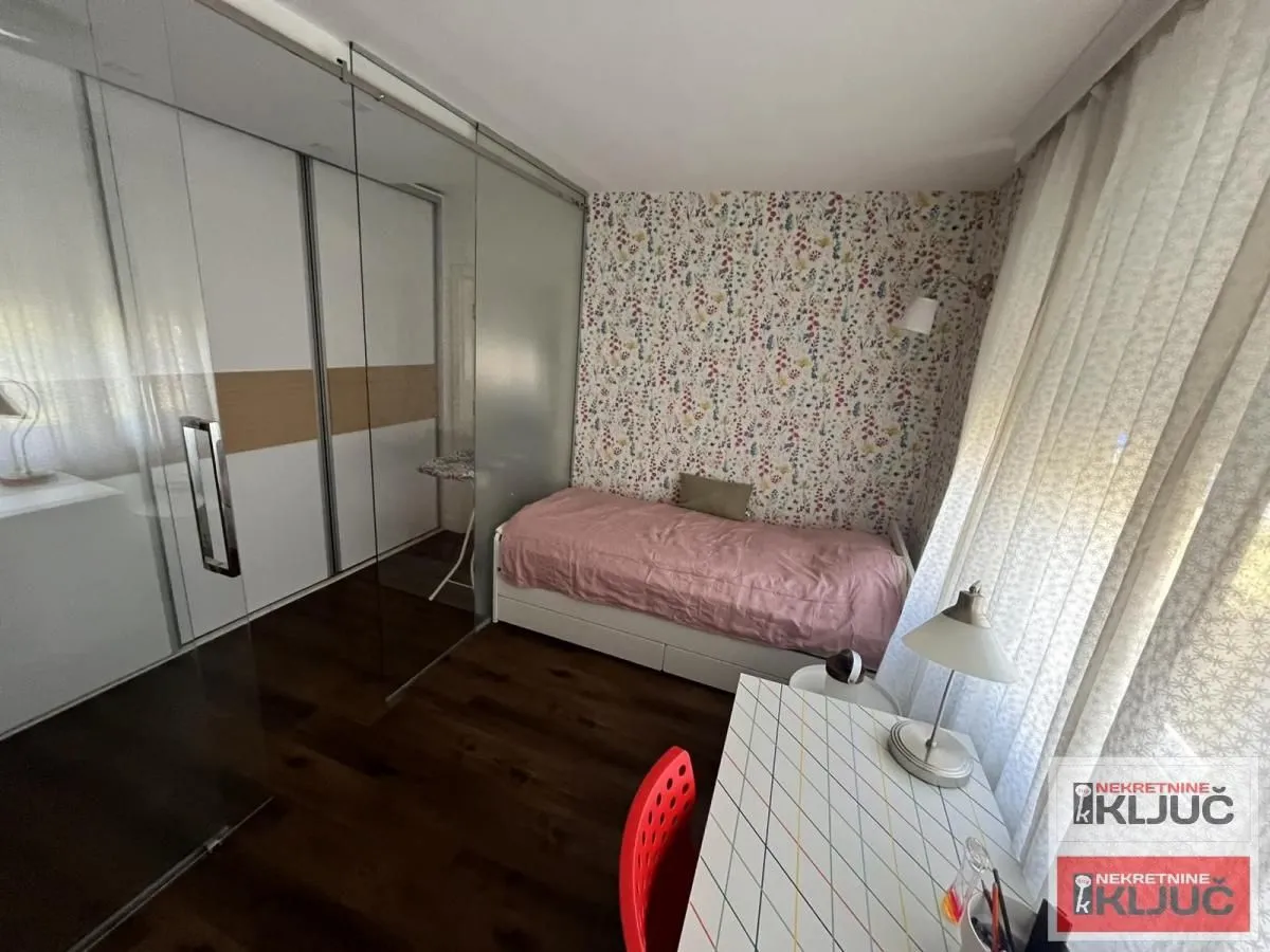 Manja spavaća soba sa krevetom, radnim stolom i velikim ugradnim garderoberom.