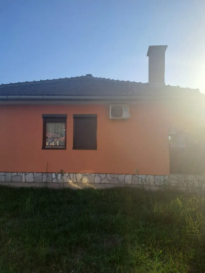 Eksterijer prizemne kuće sa narandžastom fasadom i travnjakom u dvorištu.