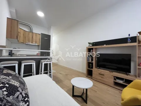 Living room with a sofa, television, and a kitchen in the background. - image 9