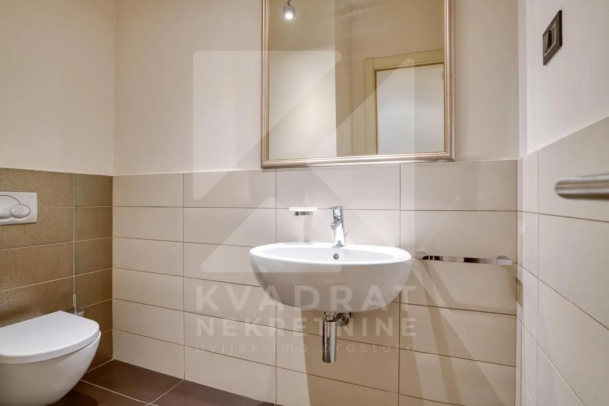 Moderne kupatilo opremljeno umivaonikom, ogledalom i WC šoljom.