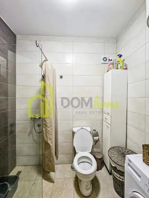 Smaller bathroom with a shower cabin, toilet, and washing machine.