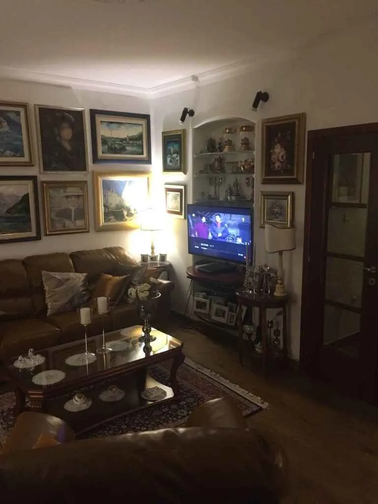 Dnevna soba sa kožnom garniturom, televizorom i brojnim umjetničkim slikama na zidu.