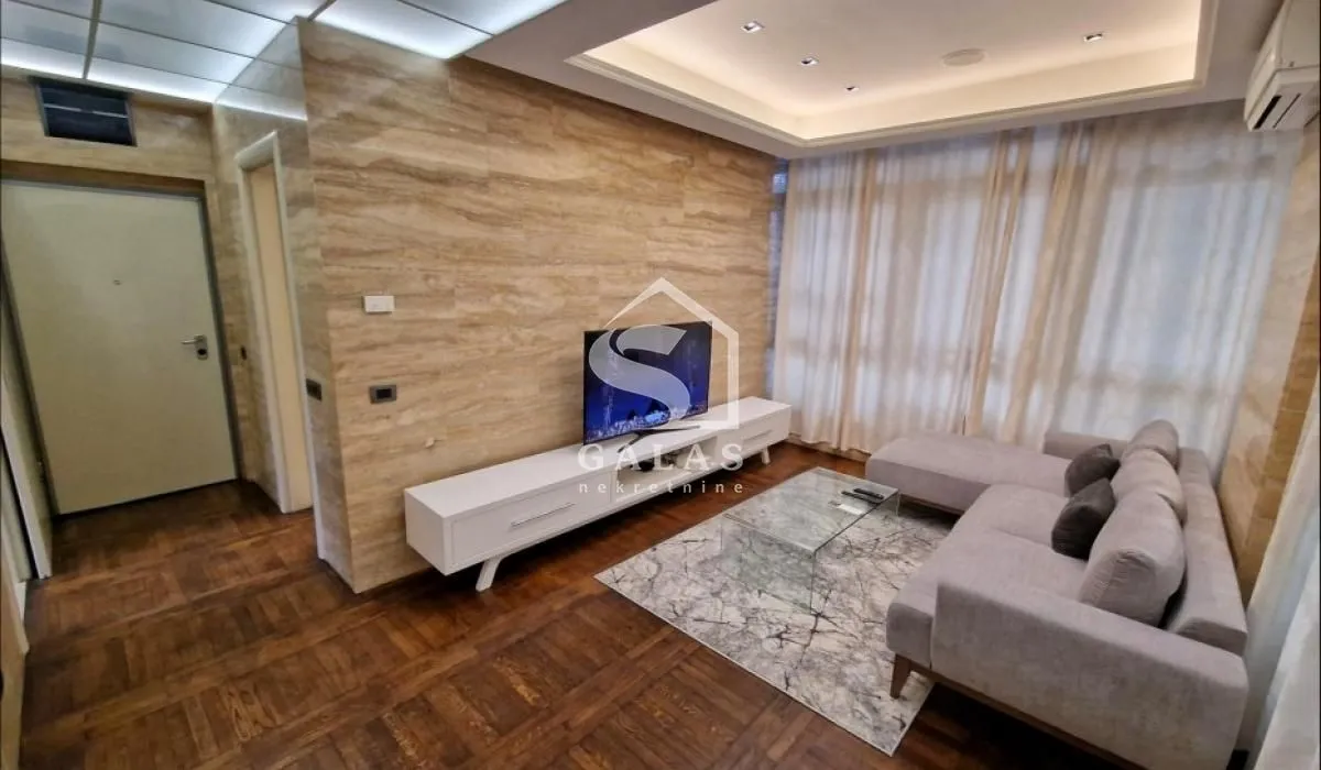 Living room with a sofa, TV, and wooden flooring.