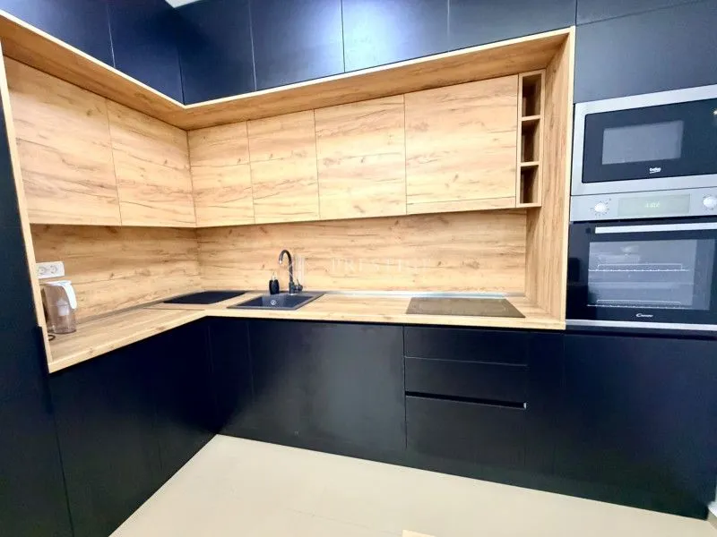 Moderna kuhinja sa tamnim elementima i drvenim detaljima.