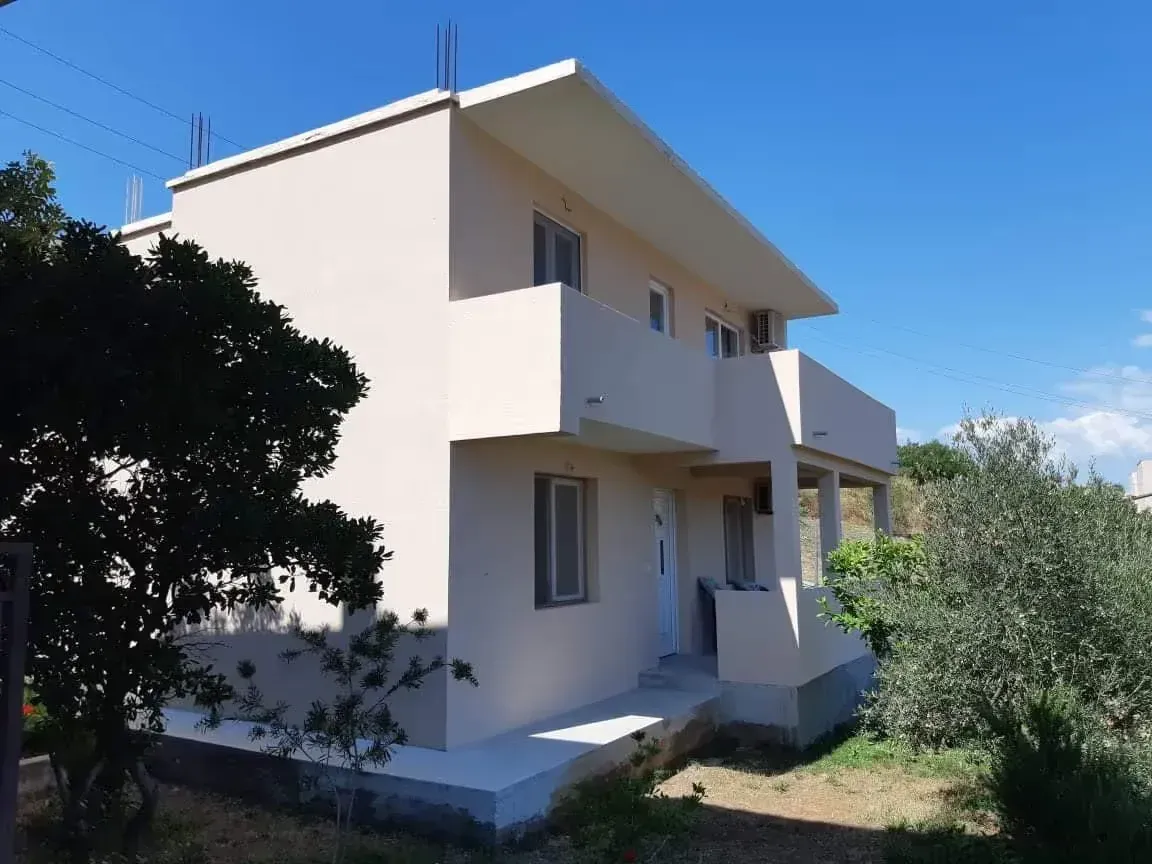 Pogled na spoljašnjost dvospratne kuće sa balkonom i dvorištem.