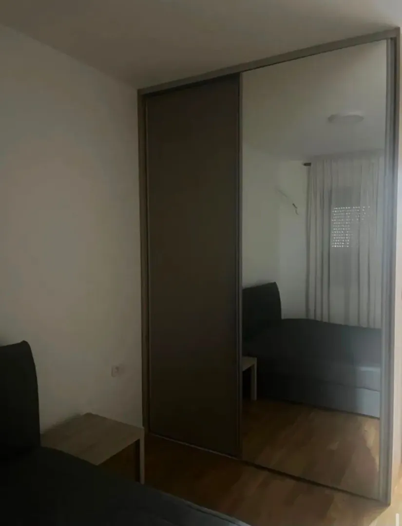 Spavaća soba sa velikim ugradnim garderoberom sa ogledalom i bračnim krevetom.