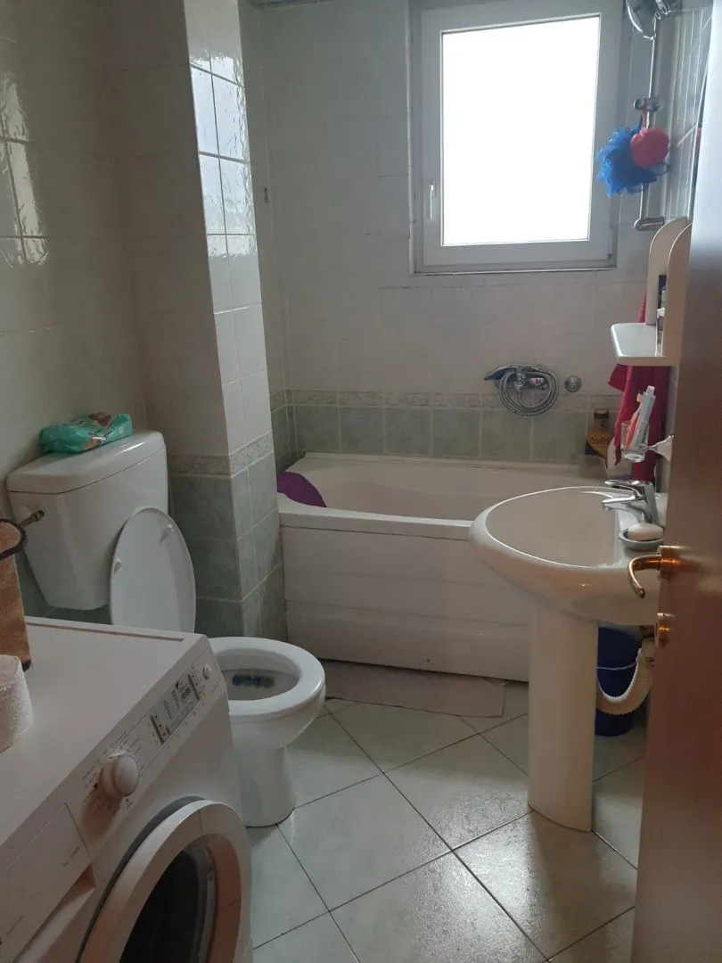 Jednostavno kupatilo sa kadom, lavaboom, toaletom i veš mašinom.