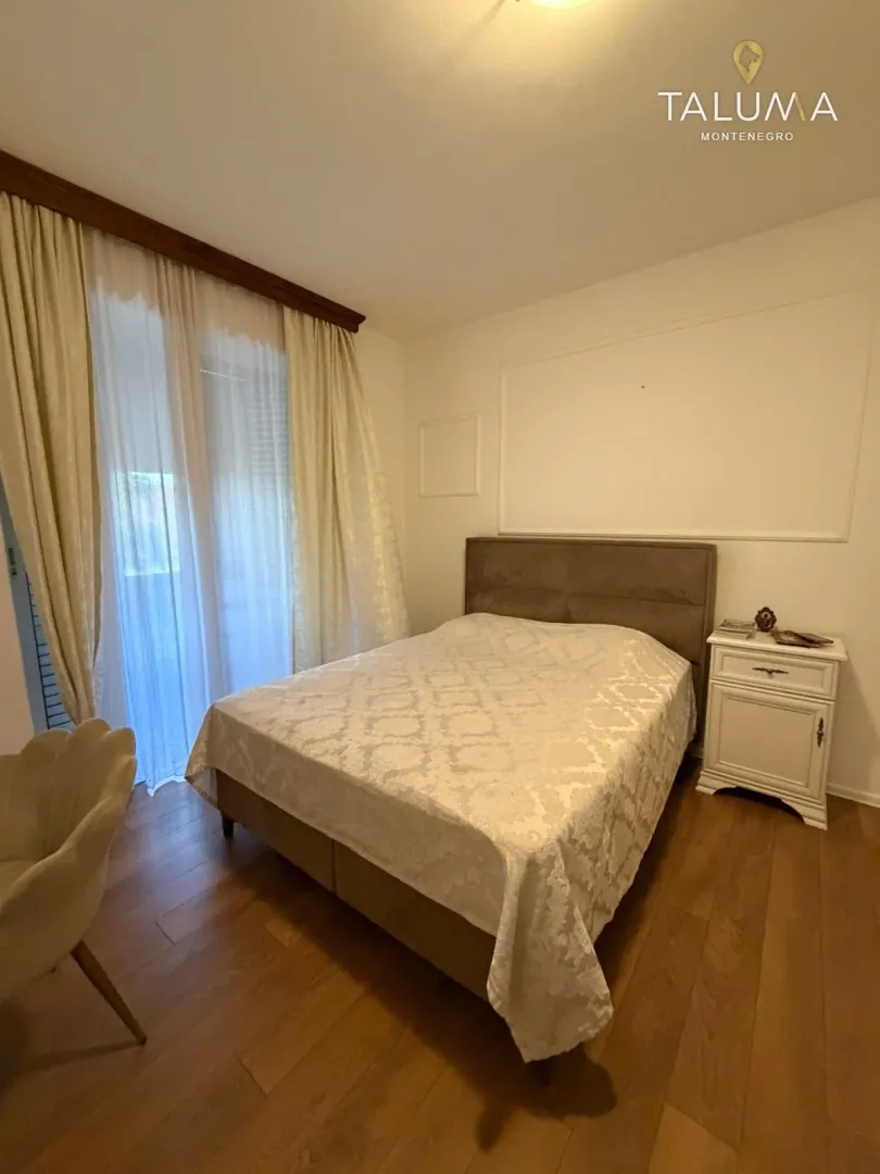 Spavaća soba sa bračnim krevetom, noćnim stočićem i balkonskim vratima.