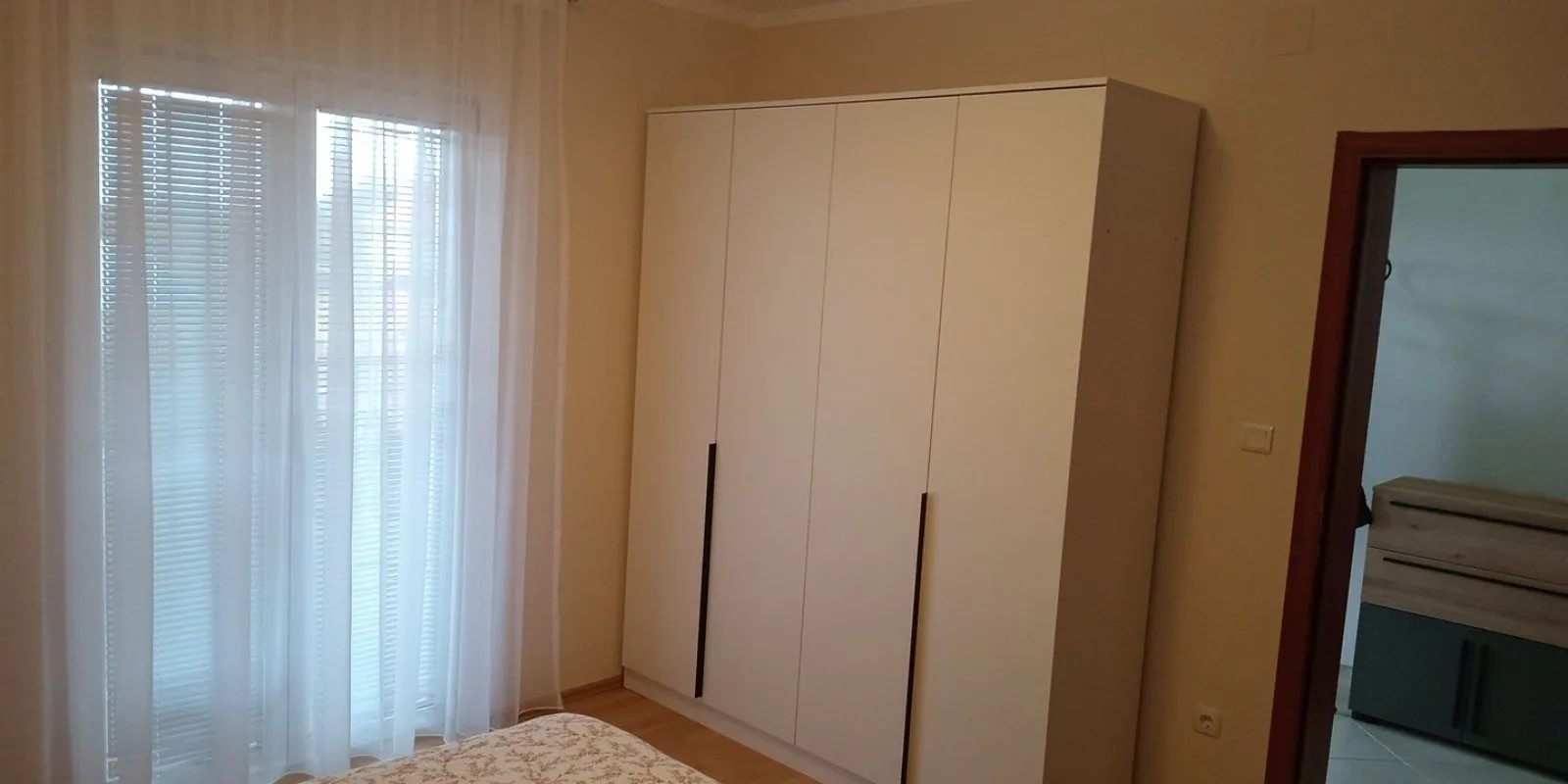 Bedroom with a large white wardrobe and a window with curtains.
