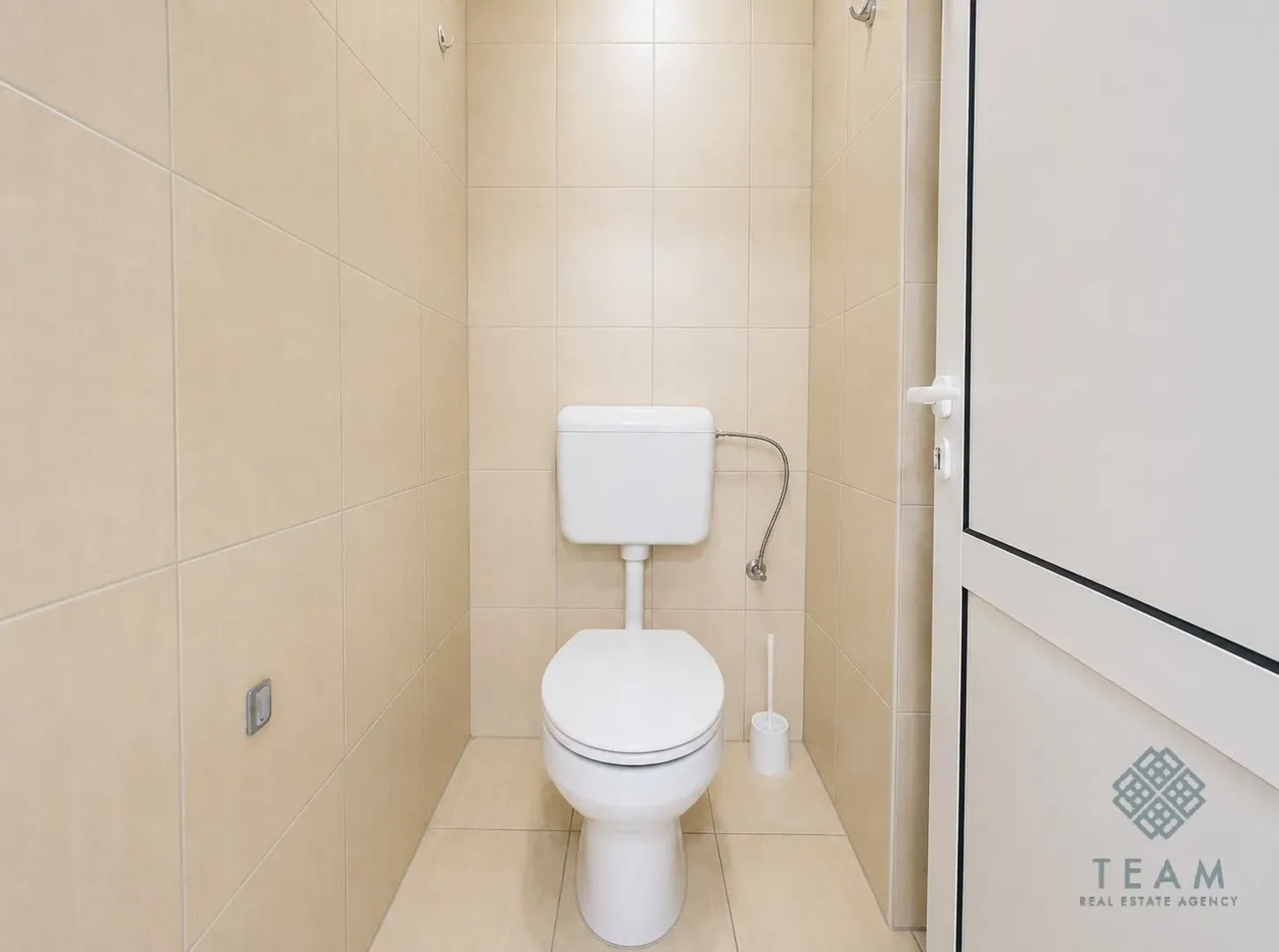 Small bathroom lined with beige tiles featuring a toilet and a door.