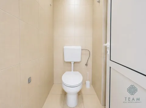 Small bathroom lined with beige tiles featuring a toilet and a door. - image 5