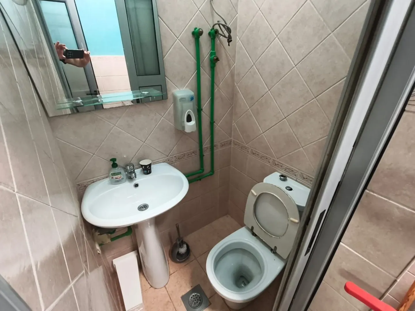 Small bathroom with a sink and toilet, tiled with ceramic tiles.