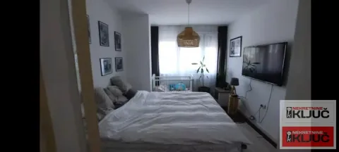 Prostrana spavaća soba sa velikim bračnim krevetom, TV-om na zidu i dečijim krevetcem u pozadini. - image 9