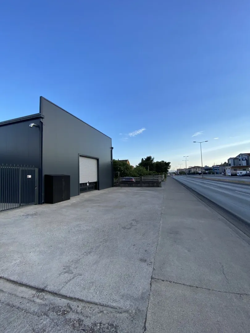 Exterior view of a modern commercial building with roller shutter doors next to a road.