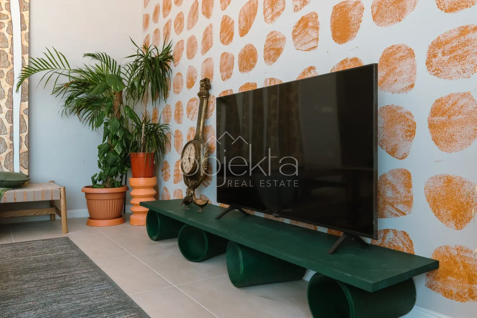 Dnevna soba sa televizorom na zelenoj komodi i ukrasnim biljkama.