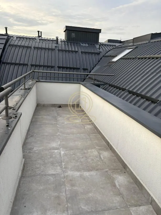 Nenamešten balkon sa popločanim podom i metalnom ogradom.