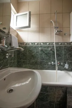 Small bathroom with a bathtub, sink, and green-toned tiles. - image 17