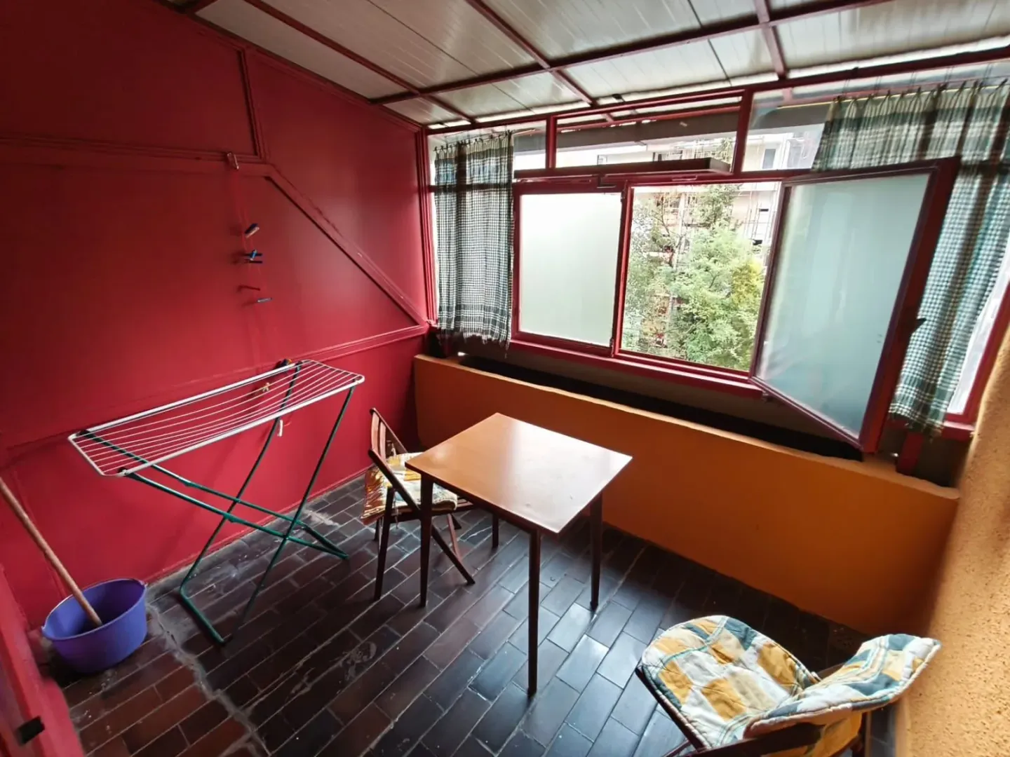 Zastakljeni balkon sa crvenim zidovima, stolom i stalkom za sušenje veša.