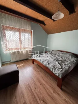 Spavaća soba sa bračnim krevetom, drvenim podom i prozorom sa zavesama. - image 4