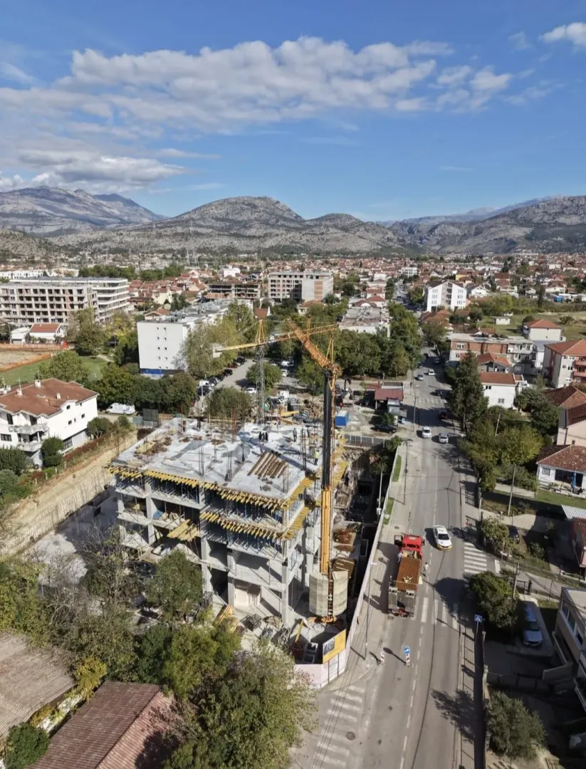 Aerial view of a residential building under construction with a crane and surrounding cityscape.