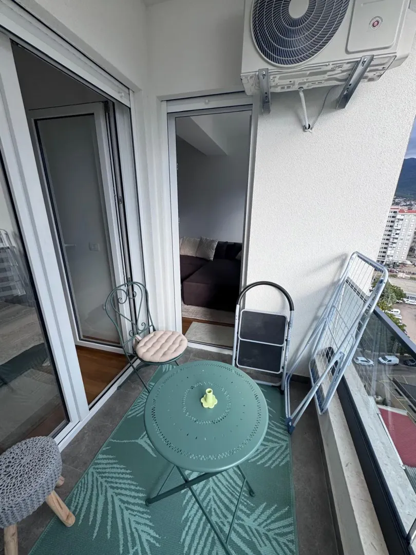 Manji namješten balkon sa stolom, stolicama i klima uređajem.